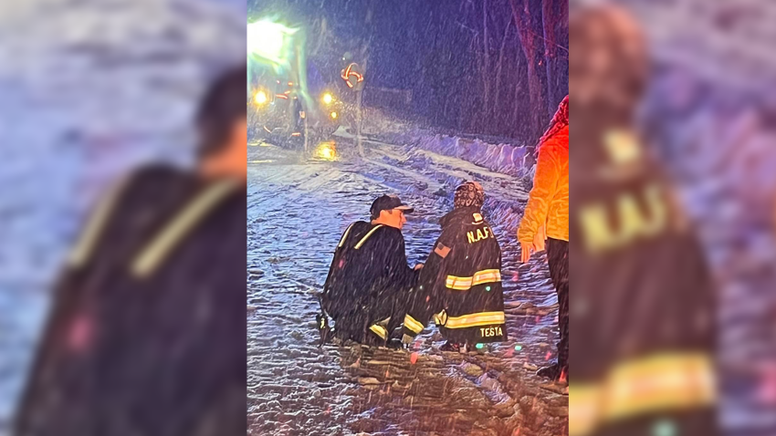 A firefighter bends down next to a child wearing his jacket in a snowstorm in North Andover, Massachusetts.